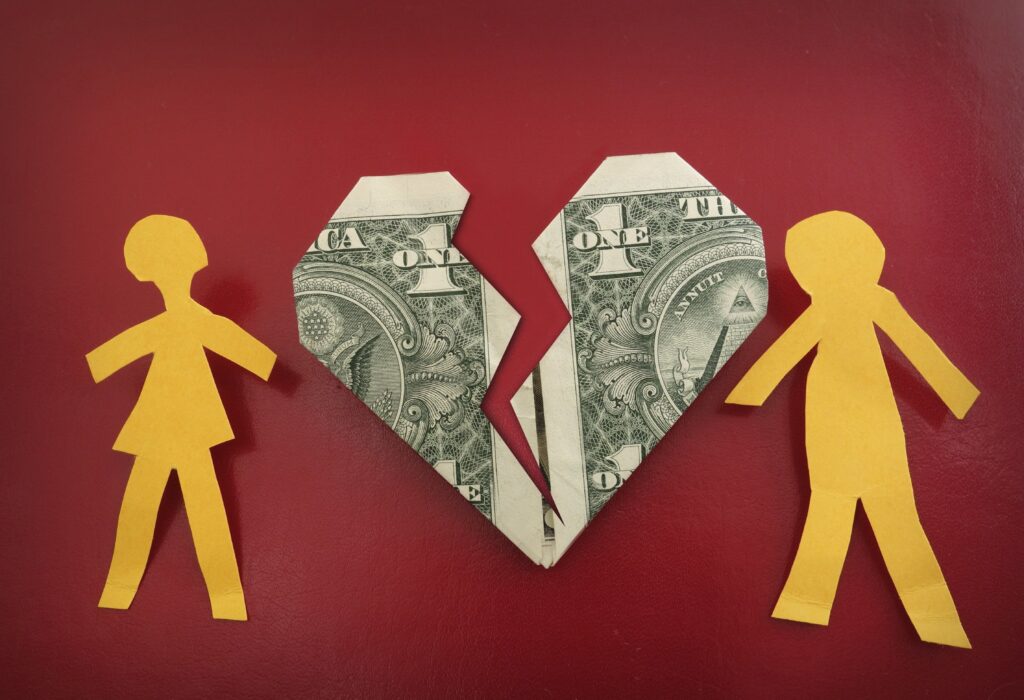 Dollar bill shaped like a broken heart with yellow cut-out images of a man and woman on each side. 