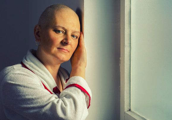 Image of a bald female cancer patient leaning against a wall.