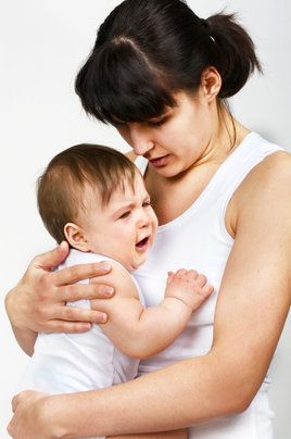 Woman in white tank top holding crying baby