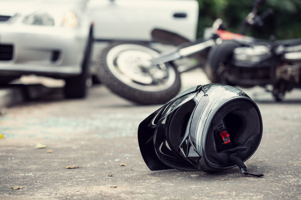 Close-up of motorcycle helmet with crashed motorcycle and car in background