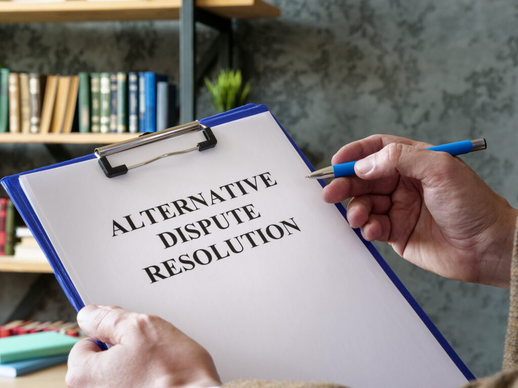 Close-up of man holding pen and blue clipboard with paper that says, “alternative dispute resolution.”