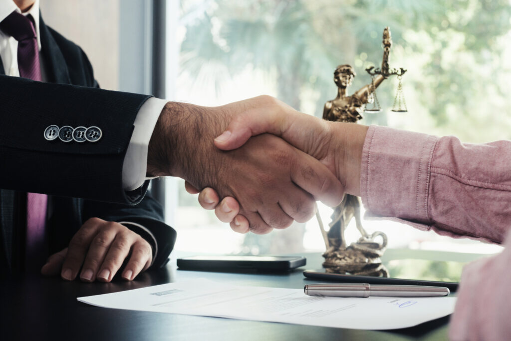 Close-up of lawyer and woman shaking hands over desk