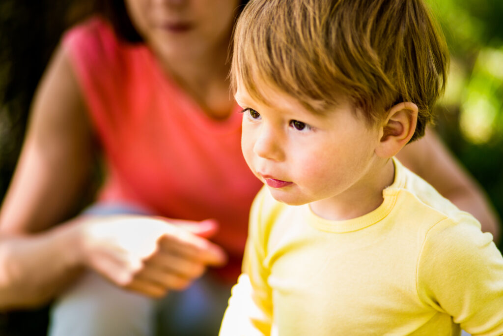 Boy in yellow shirt with blurred image of woman behind him.