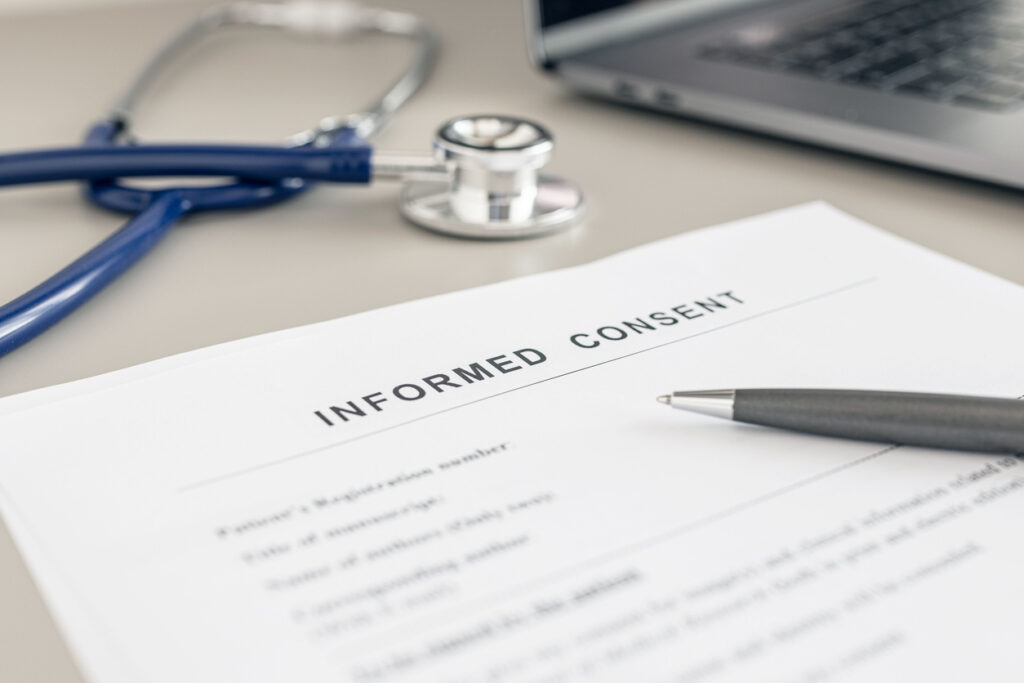 Informed consent form, pen, and stethoscope next to computer
