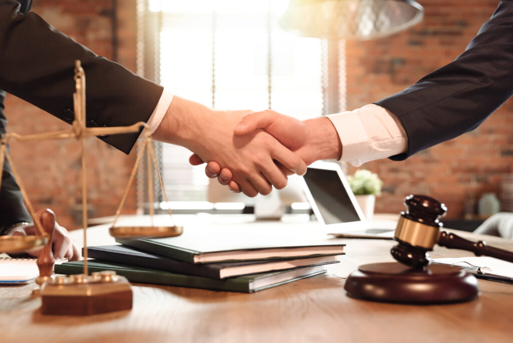 Close-up of lawyers shaking hands over desk with gavel, books, and scales of justice