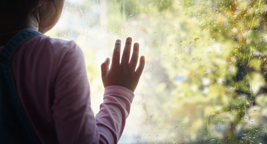Little girl looking out window on rainy day
