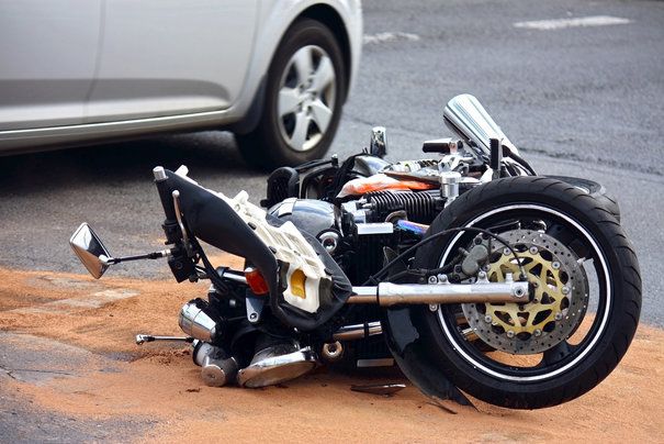 Wrecked motorcycle on ground with silver car in background